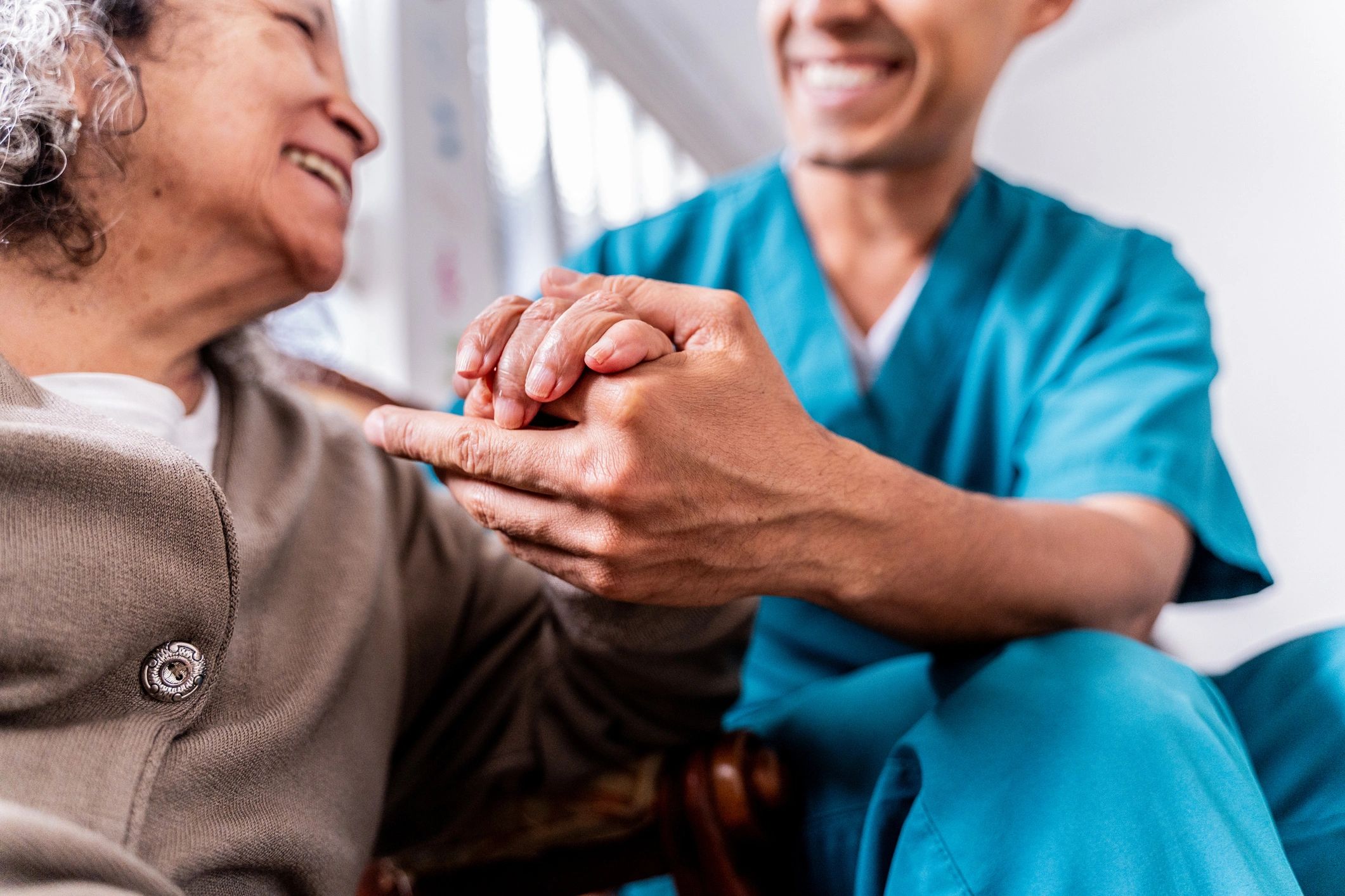 Senior woman holding a caregiver's hands at home